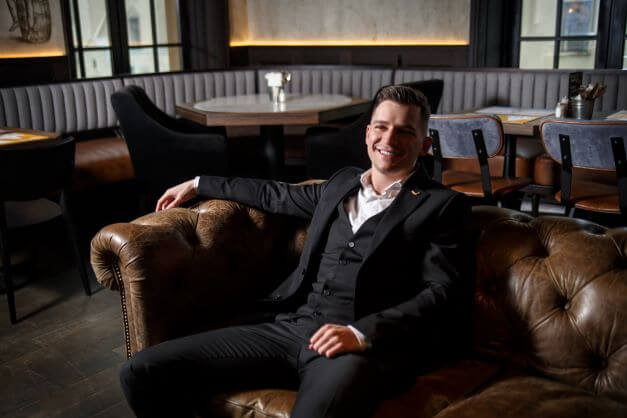 Man sitting in sofa in a three piece suit with no tie