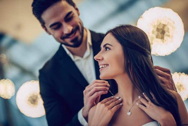 A lady with necklace being place around her neck by a man